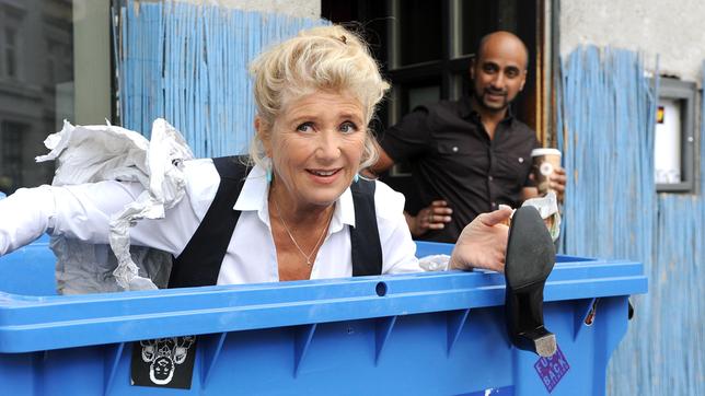 Fanny (Jutta Speidel) versteckt sich vor dem Gerichtsvollzieher in einer Papiertonne. Ihr Stammwirt Santiago (Murali Perumal) steht schon mit einem Kaffee bereit.