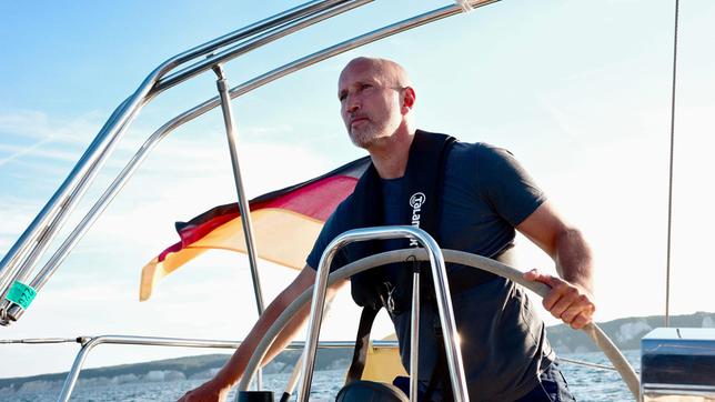 Schauspieler und Ostseeliebhaber Benno Fürmann am Steuer eines Segelschiffes auf der Ostsee während der Dreharbeiten zum Film „Ostsee am Limit“.