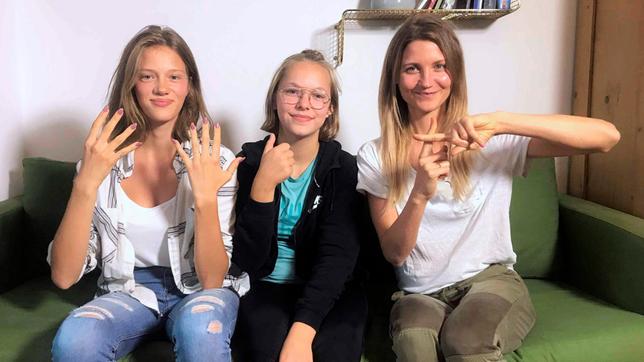 Jana sitzt mit der tauben Navina und ihrer Freundin Luana auf einer Couch. So sieht „neuneinhalb“ in Gebärdensprache aus.