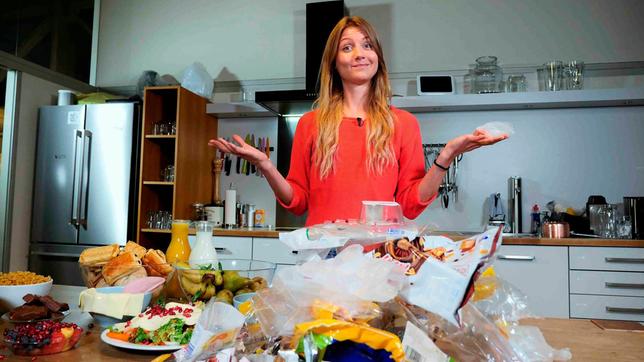 Jana steht in einer Küche hinter einem großen Haufen Plastikverpackungen.