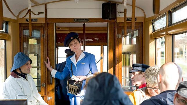 Direktor Berger (Robert Schupp) bemerkt verdutzt, dass Frau Rottbach (Angelika Böttiger) in der Tram als Schafferin arbeitet.