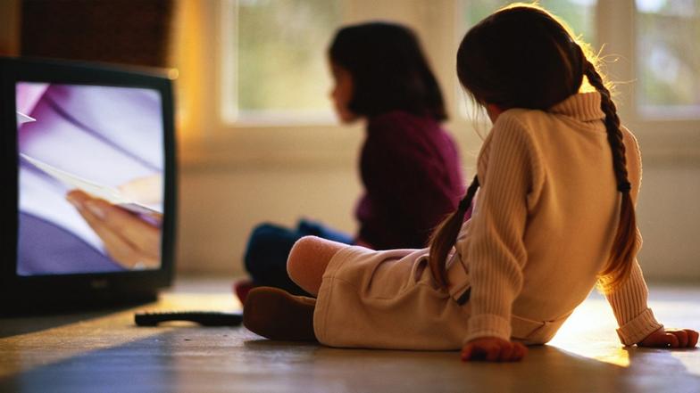 Zwei Mädchen sitzen am Boden vor einem Fernseher