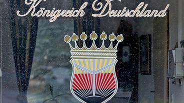 Logo des «Königreich Deutschland» (geschwungene Schrift; darunter eine Krone, u. a. in den Farben schwarz-rot-weiß) an einem Fenster