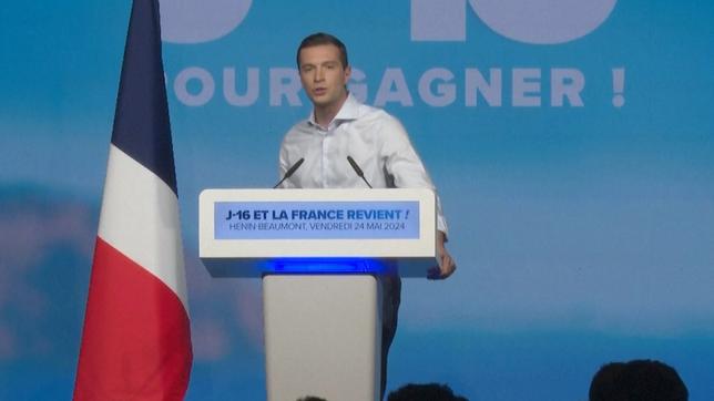 Jordan Bardella steht an einem Rednerpult, neben ihm eine französische Flagge.