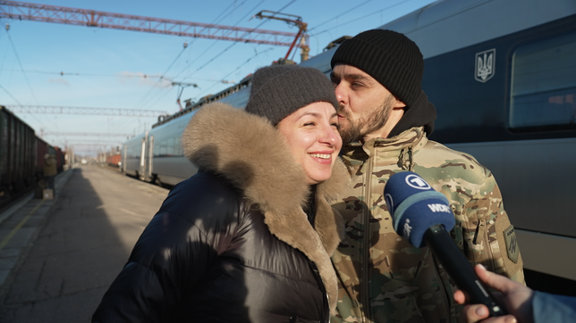 Ein Mann küsst eine Frau auf den Kopf, im Hintergrund ein Zug mit dem ukrainischen Wappen