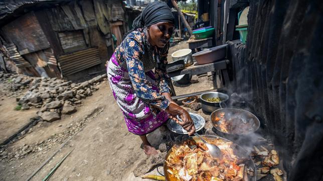 Eine Frau kocht vor einer Hütte