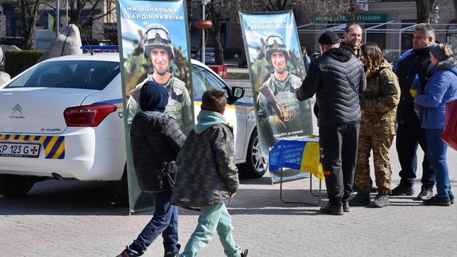 Menschen vor zwei Plakaten mit ukrainischen Soldaten
