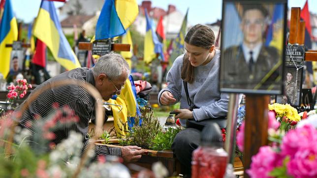 Ein älterer Mann und eine Frau kümmern sich um ein Grab auf dem Feld der Ehrengräber auf dem Lytschakiwski-Friedhof