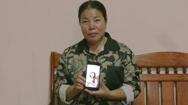 Eine Frau halt ein BIld ihrer Tochter auf dem Handy in die Kamera.