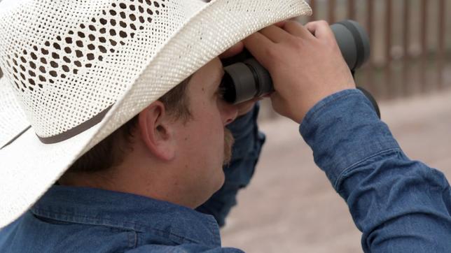 Ein Mann mit Cowboyhut schaut durch ein Fernglas.