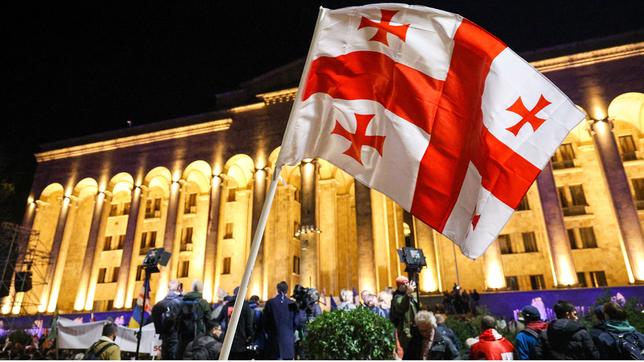 Die rot-weiße georgische Flagge wird vor dem bei Nacht erleuchteten georgischen Parlament geschwenkt.