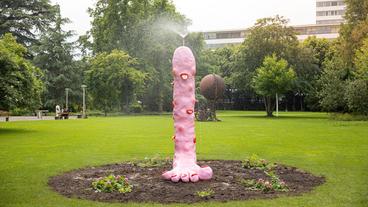 Rosafarbene, wasserspeiende Skulptur eines Fußes in einem Park.