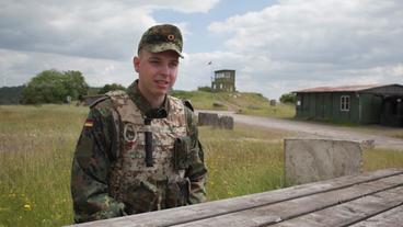 Ein Soldat sitzt auf einer Bank im Feld und wird interviewt.