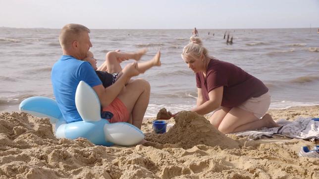 Filmausschnitt aus "Wie die Liebe geht": Eltern mit einem Kind spielen am Strand.