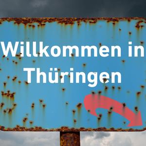 Ein blaues Schild mit Rost an den Raendern, rostigen Flecken sowie mit der Aufschrift "Willkommen in Thueringen" und einem roten Pfeil nach rechts unten an einem rostigen Schildermast vor einem grau bewoelkten Himmel mit aufziehendem Gewitter