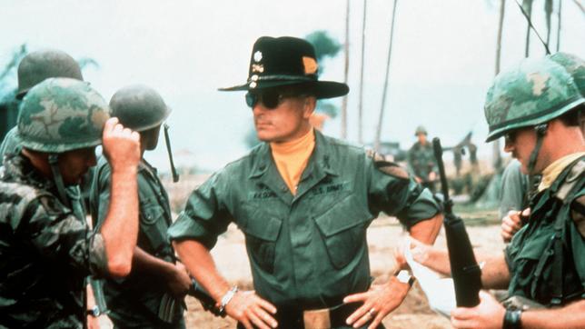 Colonel Kilgore (Robert Duvall, Mitte) erklärt Captain Willard (Martin Sheen, li.), dass er ein ganzes Dorf ausradieren will, um an einem hart umkämpften vietnamesischen Strand gefahrlos surfen zu können.