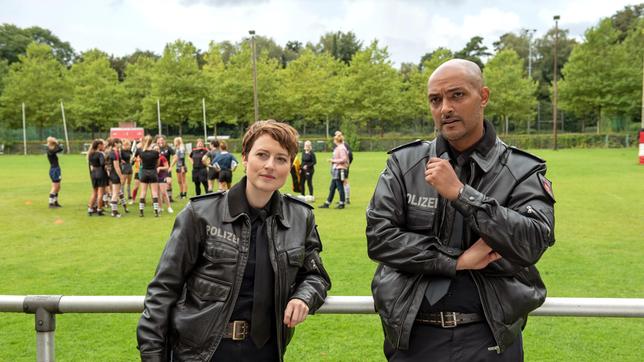 Noch spannender als das Rugby-Training der Mädchen selbst ist, was Nina Sieveking (Wanda Perdelwitz) und Lukas Petersen (Patrick Abozen, r. mit Kompars:innen, h.) abseits des Spielfeldes beobachten können.