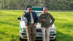 Hubert (Christian Tramitz) und Riedl (Paul Sedlmeir) lehnen am Streifenwagen und beobachten Girwidz.