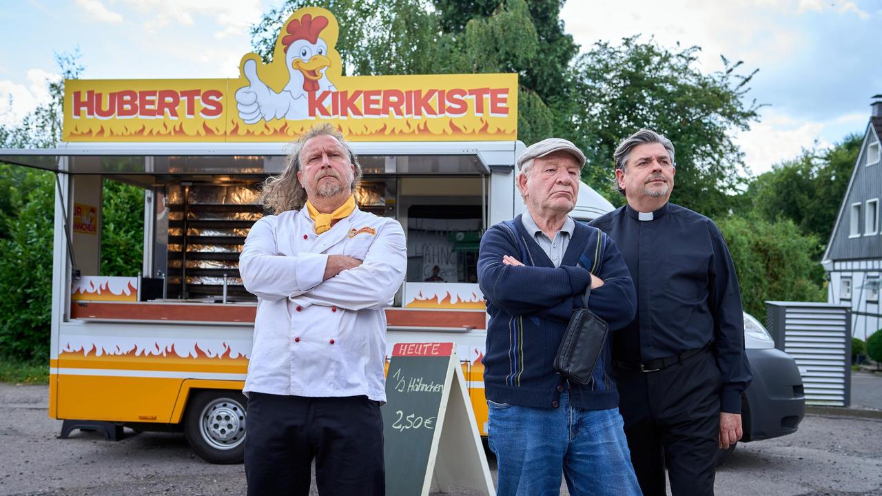 Hans Zielonka (Michael Hanemann), Pastor Puttermann (Johannes Rotter) und Hubert (Matthias Komm) stehen vor Huberts Hähnchenwagen und schauen zum "Pascha Grill", wo die Hindus ihren Gottesdienst feiern.