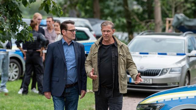 Die Kriminalhauptkommissare Lars (Ingo Naujoks) und Finn (Sven Martinek) kommen am Tatort an und diskutieren den Fall des toten Grafikers Jonas Schlebusch.