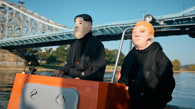 Zwei maskierte Personen, jeweils als Trump und Kim Jong Un fahren mit einem Motorboot.