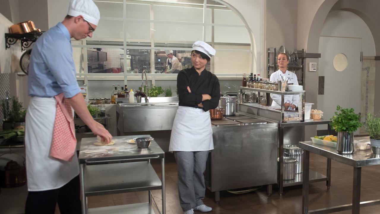 Carla (Maria Fuchs) beobachtet, wie gut Ellen (Yun Huang) ihre Aufgabe als Leiterin des Koch-Events meistert. Auch der Kursteilnehmer (Fabio Korinth) ist sehr zufrieden.