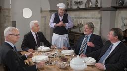 Nicos (Markus Graf) präsentiert sich vor Thomas (Gerry Hungbauer) und dessen Gästen (Komparsen) stolz als Maître de Cuisine.