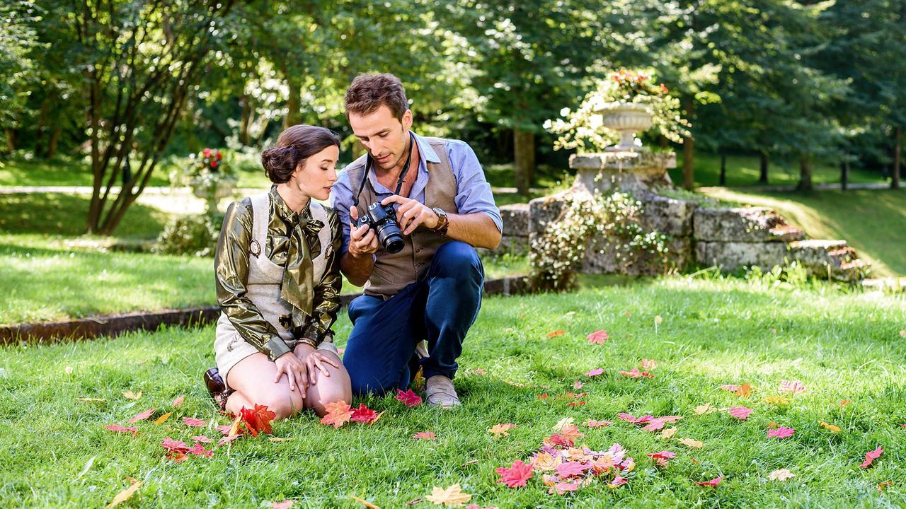 Clara und Adrian sitzen im Gras und blicken auf ein Kameradisplay.